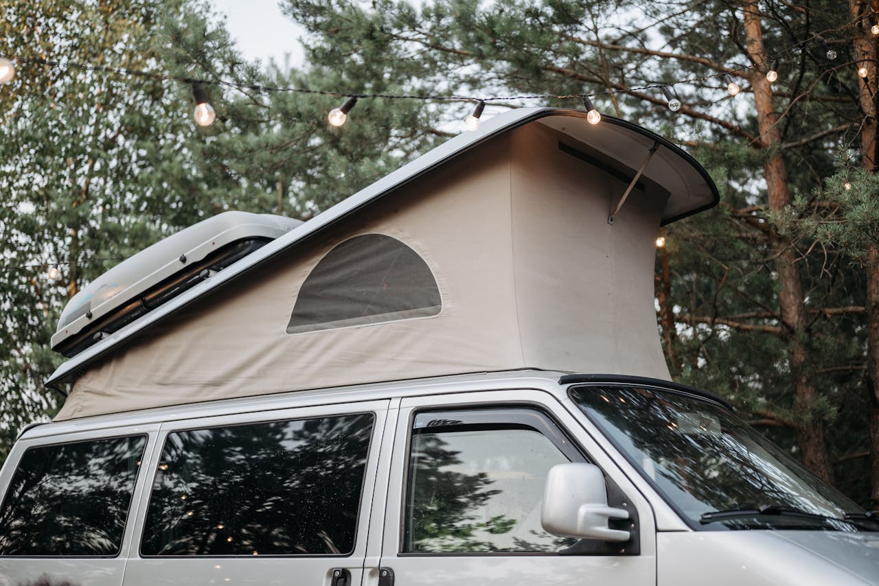 Pop-up campervan roof surrounded by string lights in a tranquil forest ambiance.